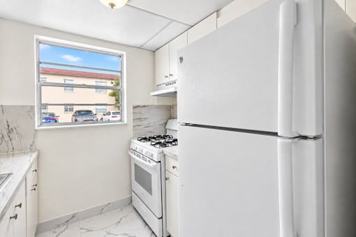 A white refrigerator stands in a kitchen with a window showing a street view.