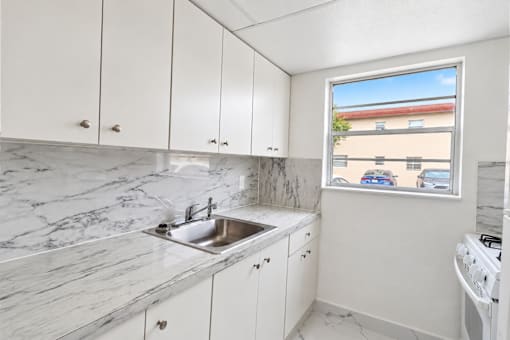 A kitchen with white cabinets and marble countertops.