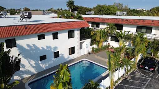 A white building with a red roof and a pool in the foreground.