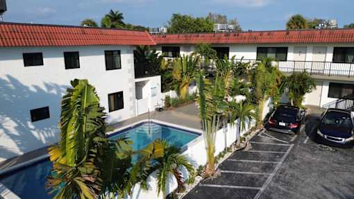 A white building with a red roof and a pool in the foreground.