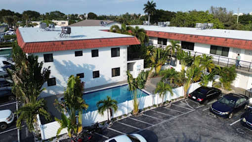 A white building with a red roof is surrounded by a parking lot.