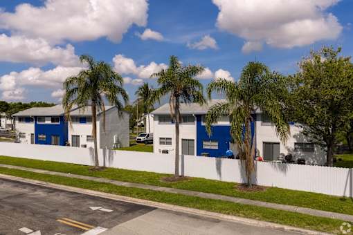 A row of palm trees in front of a blue building.