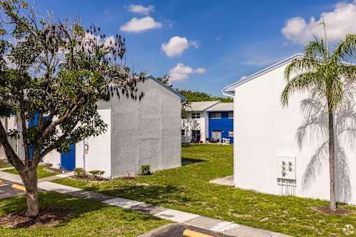A white building with a blue door and a tree in front of it.