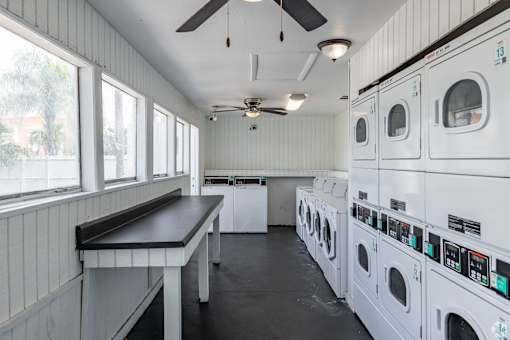 A laundromat with a row of washers and dryers on the right and a bench on the left.
