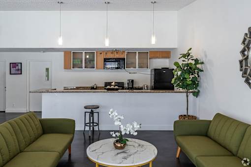 A living room with a green couch, a white coffee table, and a kitchen area in the background.