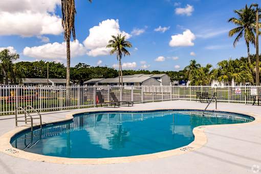 A round blue swimming pool surrounded by a fence with palm trees in the background.