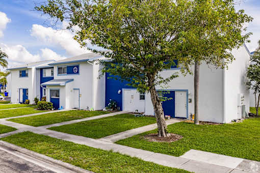 A white and blue building with a tree in front.