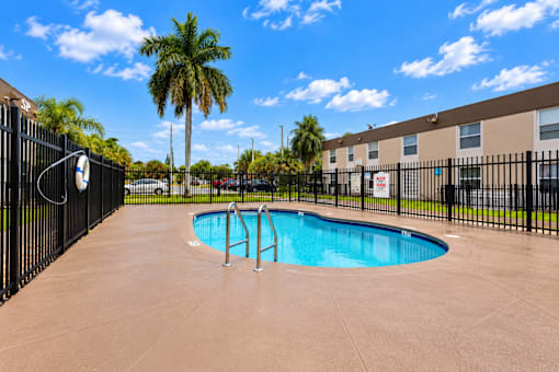 A black fence surrounds a small pool in a sunny outdoor area.