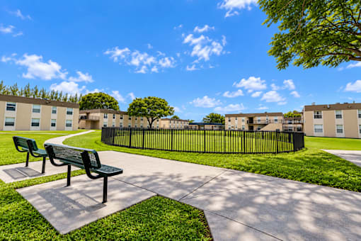 A park with benches and a fence in front of apartment buildings.
