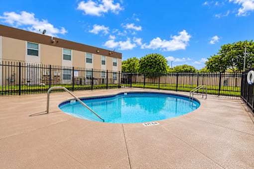 A small pool in a concrete patio surrounded by a black fence.