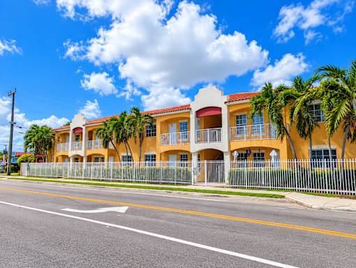A row of yellow buildings with palm trees in front.