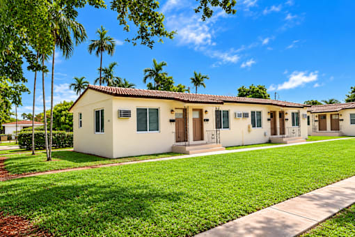 A row of houses with green lawns and trees in the background.