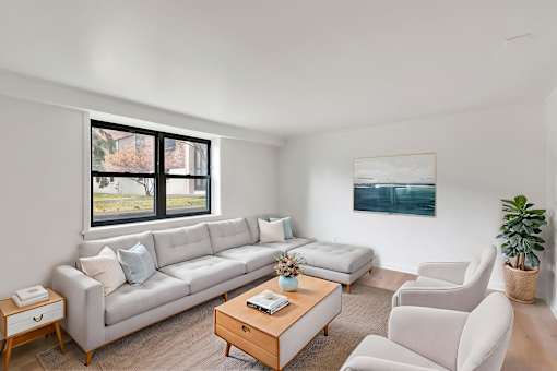 A living room with a large window, a white couch, a coffee table, and a painting on the wall.