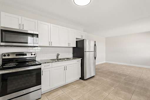 A kitchen with white cabinets and appliances, a stove, a microwave, and a refrigerator.