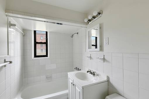A white bathroom with a tub, sink, mirror, and a window.