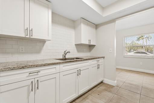 A kitchen with white cabinets and a marble countertop.