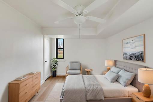 A bedroom with a large bed, a ceiling fan, and a painting on the wall.