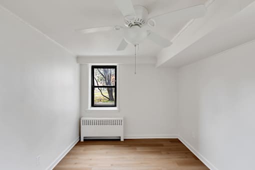 A room with a ceiling fan and a window with a view of trees.