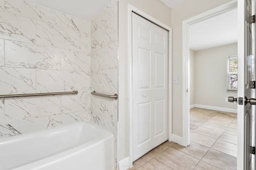 A white bathroom with a marble tile wall and a white bathtub.