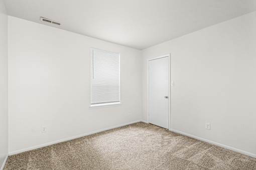 A room with a carpeted floor, a window with blinds, and a door.
