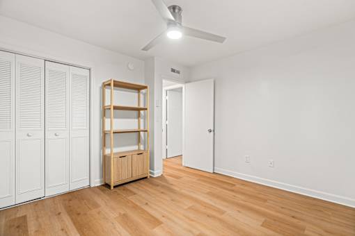 A room with a wooden floor and a white wall with a closet and a shelf.