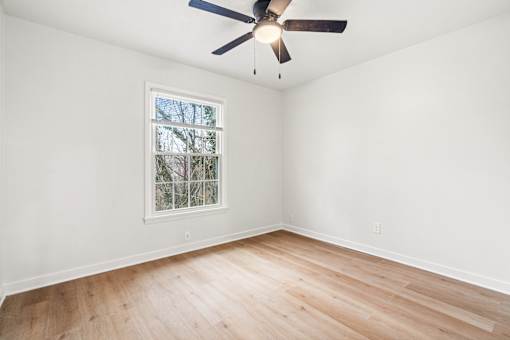 A room with a ceiling fan and a window with a view of trees.