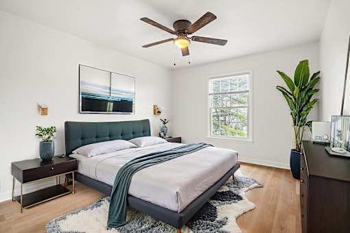 A bedroom with a bed, a ceiling fan, and a window.