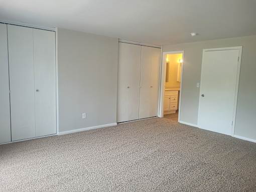A room with white walls and carpeted floor with a door on the right.