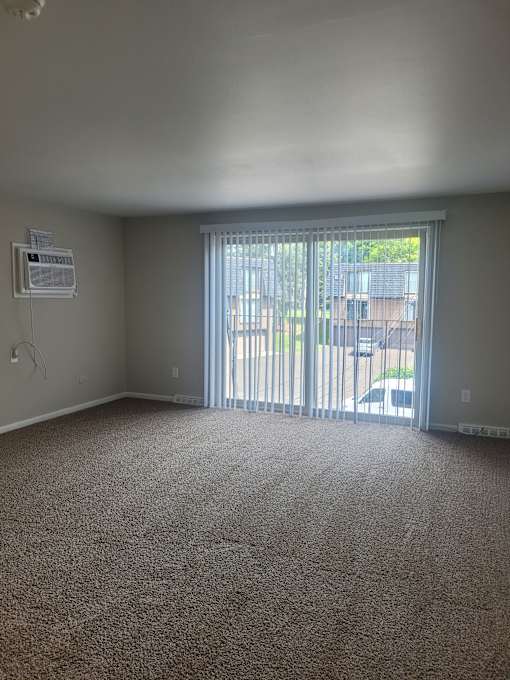 A room with a carpet floor and a window with blinds.