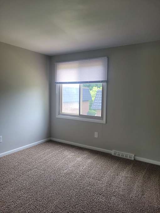 A room with a carpeted floor and a window with blinds.