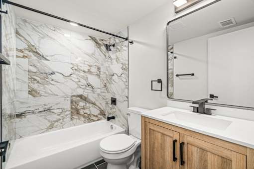 A white and marble bathroom with a toilet, sink, and bathtub.