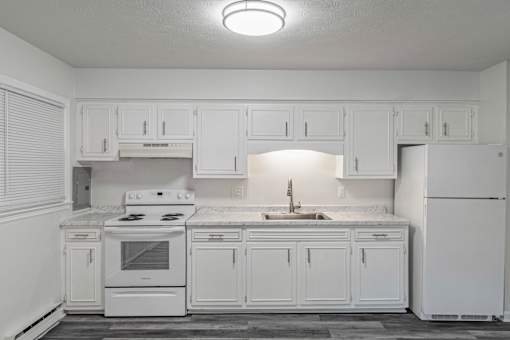 A white kitchen with a stove, sink, and cabinets.