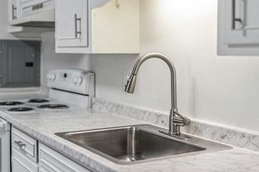 A kitchen with a stove, sink, and cabinets.