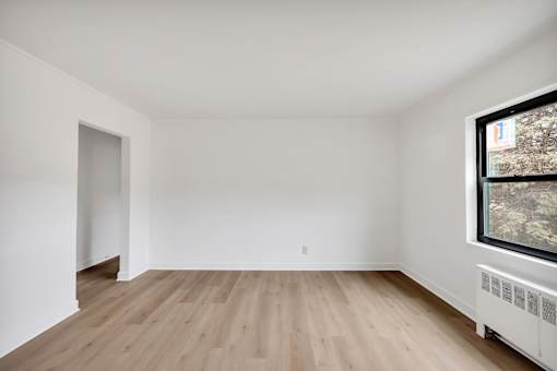 A room with wooden floors and a window showing trees outside.