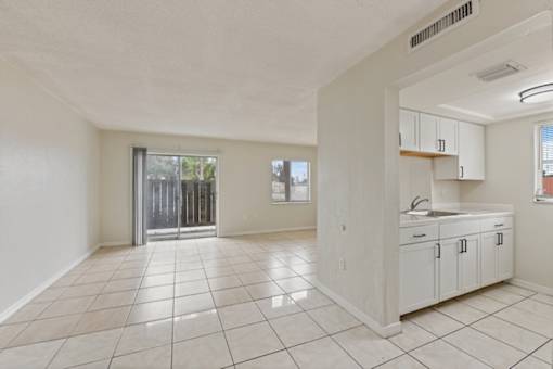 A spacious, empty room with white cabinets and a tiled floor.