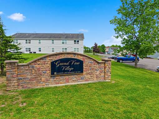 A sign that says Grand View Village is on a stone wall.
