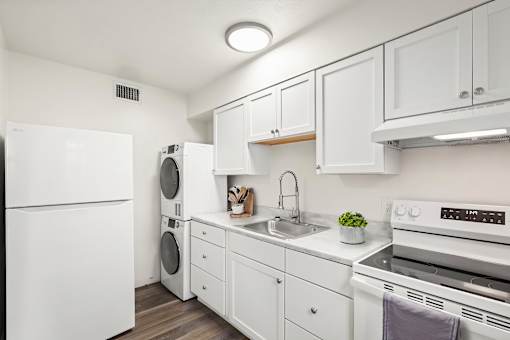 A white kitchen with a refrigerator, washing machine, dishwasher, and oven.