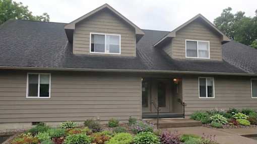 A house with a grey roof and a grey wall with a small garden in front.