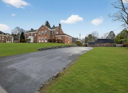 A large brick house with a long driveway in front.