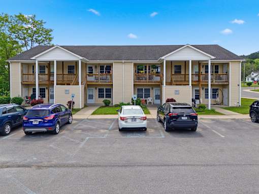 A carport with several cars parked in front of a two-story building.