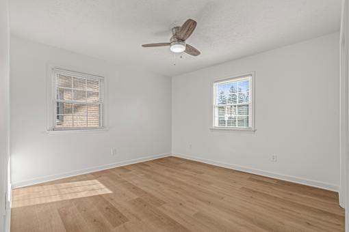A room with a ceiling fan and two windows.
