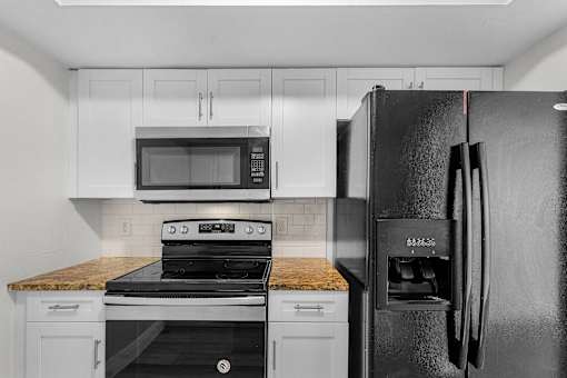A black refrigerator stands in a kitchen with white cabinets and a stove top oven.