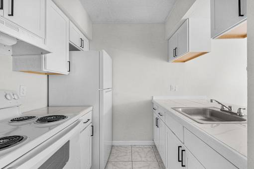A white kitchen with a stove, sink, and cabinets.
