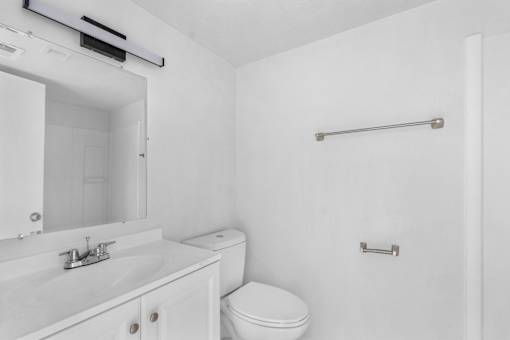 A white bathroom with a toilet, sink, mirror, and towel bar.
