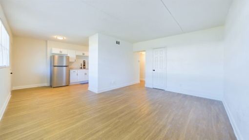 A kitchen with a refrigerator, sink, and cabinets is visible from the living room.