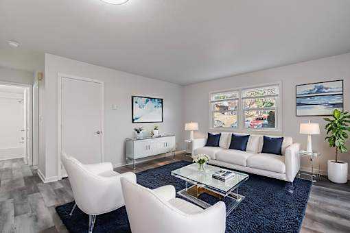A modern living room with a white sofa, two white chairs, and a glass coffee table.