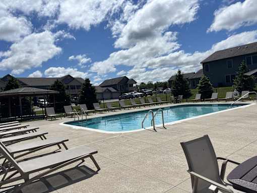 A pool surrounded by chairs and trees.