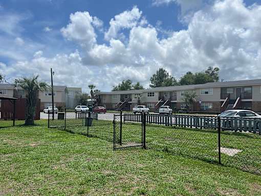 A black fence surrounds a grassy area in front of apartment buildings.