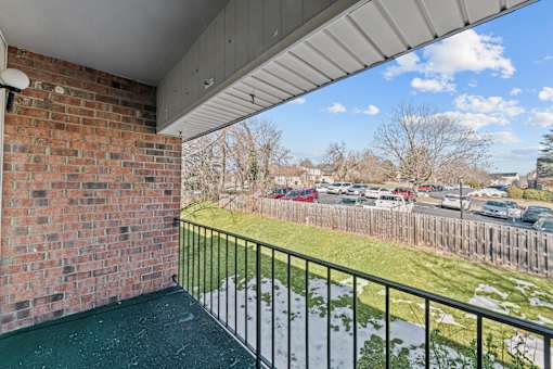 A balcony with a brick wall and a metal railing overlooking a parking lot.