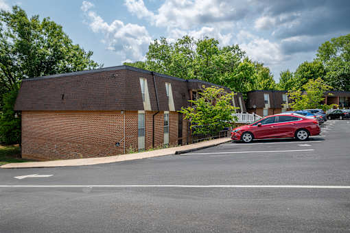 A red car is parked in a parking lot in front of a building.